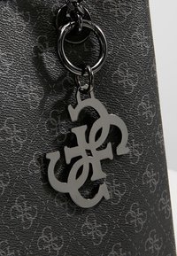 Sac en cuir noir texturé avec une surface à motifs et un charm métallique brillant avec des lettres entrelacées suspendu à un anneau métallique.