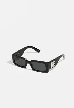 Occhiali da sole rettangolari neri con lenti scure e una montatura spessa. Presentano un dettaglio con logo impreziosito da strass sulla asta.