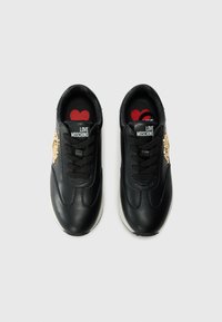 Zwarte leren sneakers met een witte zool, voorzien van zwarte veters, gouden hardware accenten en een rood hartdesign op de binnenzool.