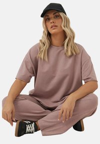 Lichtroze oversized t-shirt en bijpassende broek, met een zachte textuur. Een zwarte pet en zwarte sneakers met witte veters maken de outfit compleet.