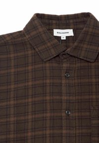 Braun kariertes Hemd aus weich texturiertem Stoff, mit einem Button-Down-Kragen und schwarzen Knöpfen entlang der Vorderseite.