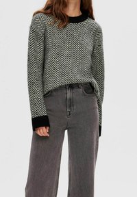 Zwart-grijs trui met een chevronpatroon, een geribde zwarte halslijn en manchetten, gecombineerd met een grijze high-waist spijkerbroek.