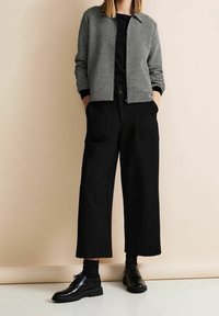 Szary, teksturowany żakiet z kołnierzem, czarna koszula pod spodem, szerokie czarne spodnie i czarne półbuty z sznurowadłami. Kieszenie w spodniach.