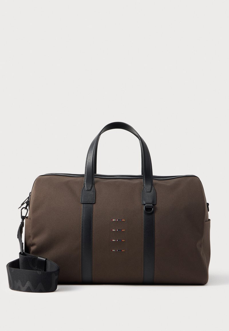 Brązowa torba podróżna z czarnymi skórzanymi uchwytami, regulowanym paskiem na ramię i małymi wielokolorowymi poziomymi przeszyciami z przodu.