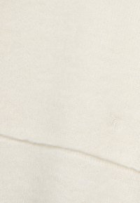 Pull en maille couleur crème avec une texture douce, présentant un logo cousu dans le coin inférieur droit et un design simple et sans coutures.