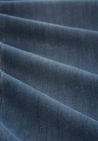Denim tkanina v temno indigo barvi z mehkobo, ki ima vertikalne gube ali pregibe, prikazuje gladko, enakomerno površino.