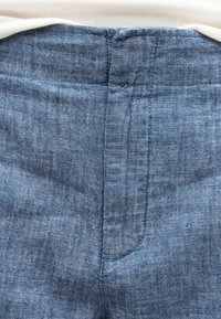 Gros plan sur un tissu en denim bleu avec des coutures détaillées sur une poche arrière et la ceinture d'un pantalon.