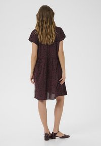 Robe à motif bordeaux avec des manches courtes, une taille froncée et une jupe évasée ; assortie à des chaussures à petit talon marron foncé.