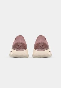 Zapatillas deportivas en rosa suave y beige pálido. Cuentan con una parte superior texturizada con perforaciones, suela de goma y un logotipo distintivo en el talón.