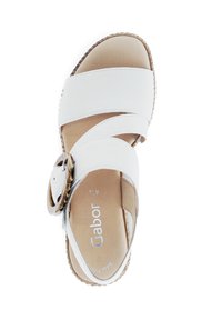 White leather sandal featuring crossed straps, a round decorative buckle, and a textured sole. Inside shows a beige footbed with branding.