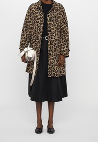 Leopardmönstrad kappa med knappstängning, kombinerad med svart topp och kjol. Inkluderar en liten vit axelremsväska och svarta ballerinaskor.