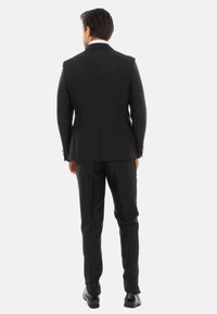 Completo nero con una silhouette aderente, spacco singolo sul retro e pantaloni eleganti. Completato con scarpe da cerimonia coordinate e una camicia formale.