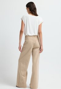 Beige wijde broek met een hoge taille, zijsnapsluitingen en twee achterzakken. Gecombineerd met een witte, korte mouwen top.