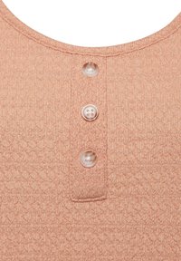Roze textuur top met een ronde hals en vier decoratieve knopen. De stof heeft een subtiel geometrisch patroon en een zachte afwerking.