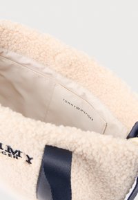 Beežikarva pehme käekott mereväesiniste käepidemete ja logoga. Siseküljel on sile vooder ning nähtav kaubamärgi silt.