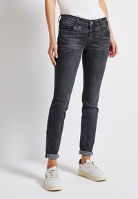 Musta slim-fit farkut, joissa on vaalea pesuefekti, viisi taskua ja käärityt lahkeet. Yhdistetty valkoisiin lenkkareihin.