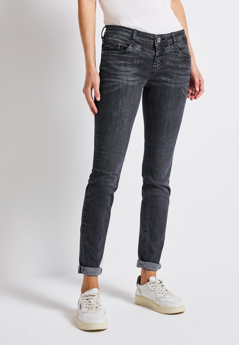 Musta slim-fit farkut, joissa on vaalea pesuefekti, viisi taskua ja käärityt lahkeet. Yhdistetty valkoisiin lenkkareihin.