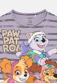 Fioletowy t-shirt w paski z napisem "PAW PATROL" w błyszczącym złocie. Ilustrowane postacie o różnych kolorach futra i akcesoriach są wyraźnie widoczne.