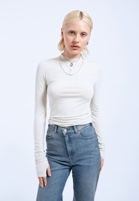 Long-sleeve, cream-colored top made from soft material with a fitted design. Paired with high-waisted, light blue denim jeans featuring a button closure.