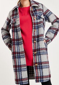 Cappotto di lana a quadri grigio, rosso e blu, con chiusura a bottoni, colletto e tasche laterali. Tessuto morbido e silhouette dritta.