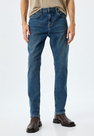 Jeans in denim blu con un design a gamba dritta, caratterizzati da un classico stile a cinque tasche e una finitura scolorita. Indossati con stivali in pelle marrone.