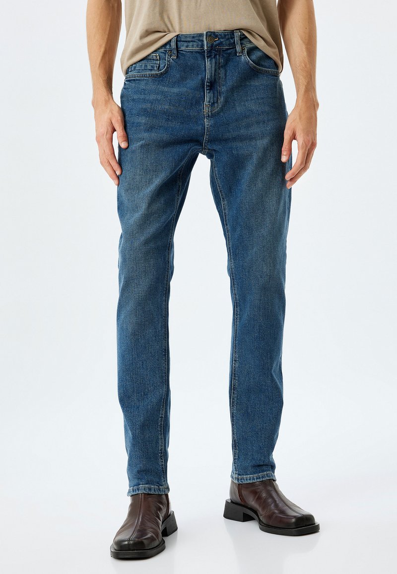 Vaqueros de denim azul con diseño de pierna recta, que presentan un estilo clásico de cinco bolsillos y un acabado deslavado. Llevados con botas de cuero marrón.
