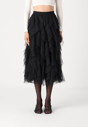 Black tulle skirt with layered ruffles, shimmering accents, elastic waistband, mid-calf length, paired with black strappy heels.