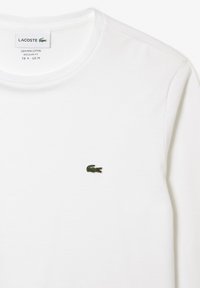 Hvid langærmet T-shirt i Pima-bomuld med rund hals og en lille grøn Lacoste-krokodille-logo broderet på venstre bryst.