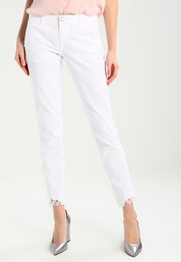 Vita beskurna jeans med spetsdetaljer vid fållen, med en tajt design, femficksstil och frontknäppning.