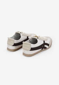 Zapatillas elegantes de cuero blanco con detalles en marrón oscuro, que presentan una puntera redonda, cordones en la parte delantera y una suela de goma texturizada.