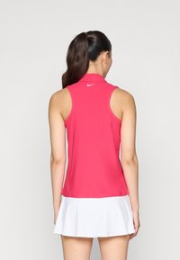 Ružový bezrukávový polo tričko s golierom, hladký materiál a jemné logo Nike na chrbte; kombinované s bielou rozšírenou sukňou.