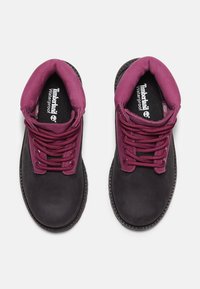 Botas impermeables negras con un cuello acolchado morado y cordones a juego. Hechas de material liso, con una suela texturizada y un logotipo en la plantilla.