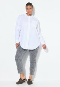 Bílá košile na knoflíky s kapsou na prsou, kombinovaná se šedými džíny s leopardím potiskem a hnědými nazouvacími botami. Jednoduchý, ležérní outfit.