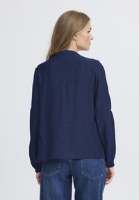 Camicia a maniche lunghe blu navy con vestibilità rilassata, tessuto testurizzato e orlo arrotondato, abbinata a jeans in denim blu.