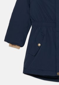 Chaqueta de invierno azul marino con cintura ceñida, puños elásticos y un bolsillo lateral con un detalle de botón plateado. Textura suave.