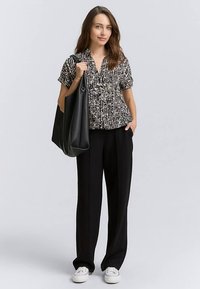 Zwart-wit blouse met patroon en korte mouwen, gecombineerd met zwarte broek met wijde pijpen en een grote zwarte tote bag. Witte sneakers maken de look af.