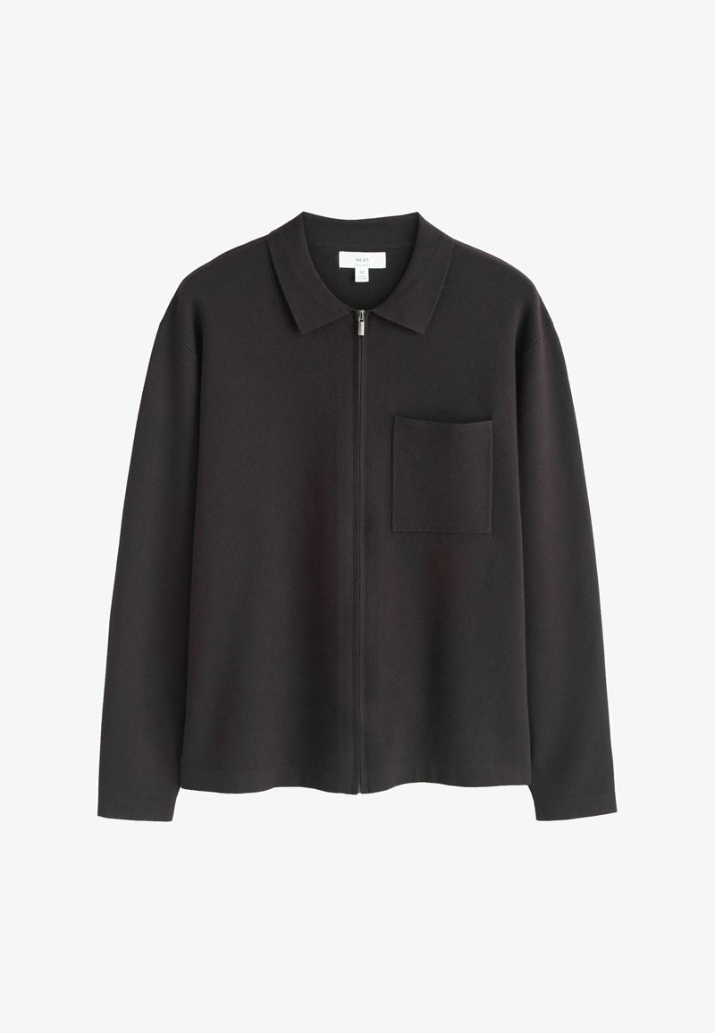 Veste noire à manches longues avec fermeture éclair, col et poche poitrine, en tissu doux, taille moyenne, étiquette de marque visible à l'intérieur du col.