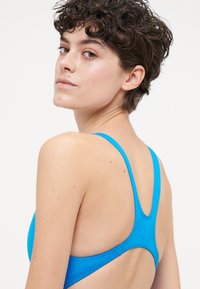 Blå sportbehå med tunna axelband och racerback-design. Slät, elastisk material med en enfärgad yta och rena sömmar.