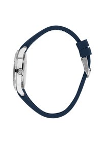 Cassa dell'orologio in argento con cinturino in silicone blu; quadrante rotondo, lunetta texture e una corona sul lato. Finitura liscia, branding sottile.