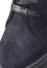 Baskets en suede bleu marine avec une surface texturée, dotées d'une plaque logo métallique noire, de coutures contrastantes et d'une semelle en caoutchouc.