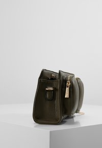 Olijfgroen leren handtas met een gestructureerde afwerking, twee compartimenten, gouden ritsdetails en een afneembare tag.
