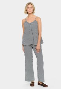 Set di pigiama a righe bianche e nere composto da una canotta morbida e ampia con spalline sottili e pantaloni a gamba larga. Tessuto morbido con un design fluido.