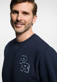 Granatowysweatshirt z okrągłym dekoltem. Posiada haftowane logo "PR" w kontrastowym białym ściegu. Miękka tkanina, luźny krój i minimalne szwy.