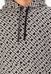 Black and white hoodie featuring a geometric pattern, drawstrings with metallic tips, and a small logo detail on the front.