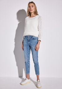 Suéter blanco de punto con un patrón texturizado, combinado con unos jeans ajustados azul claro y zapatillas blancas. Diseño simple, apariencia casual.