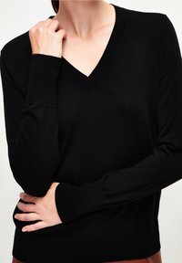 Svart, långärmad tröja med V-ringning och ribbade muddar. Mjuk stickad textur, avslappnad passform och rak nederdel. Minimalistisk design.
