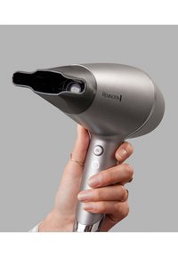 Ασημένιο πιστολάκι μαλλιών με κομψό σχεδιασμό, κυκλική μύτη και υφή στην λαβή. Διαθέτει κουμπιά στη λαβή και ένα λογότυπο στο σώμα.