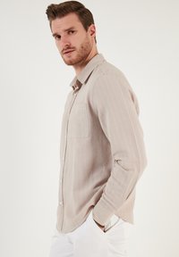 Helles beige Langarmhemd aus strukturiertem Stoff mit durchgeknöpftem Frontverschluss, einer einzelnen Brusttasche und einem weichen, lässigen Schnitt.
