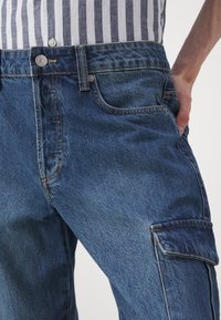 Denim cargo bukser i mørkeblå med normal pasform. Funktioner inkluderer en frontknaplukning, fire lommer og synlige syninger.
