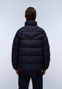 Chaqueta de plumas en azul marino oscuro, caracterizada por un diseño grueso y acolchado con secciones horizontales y un cuello alto. Textura suave y acentos mínimos.
